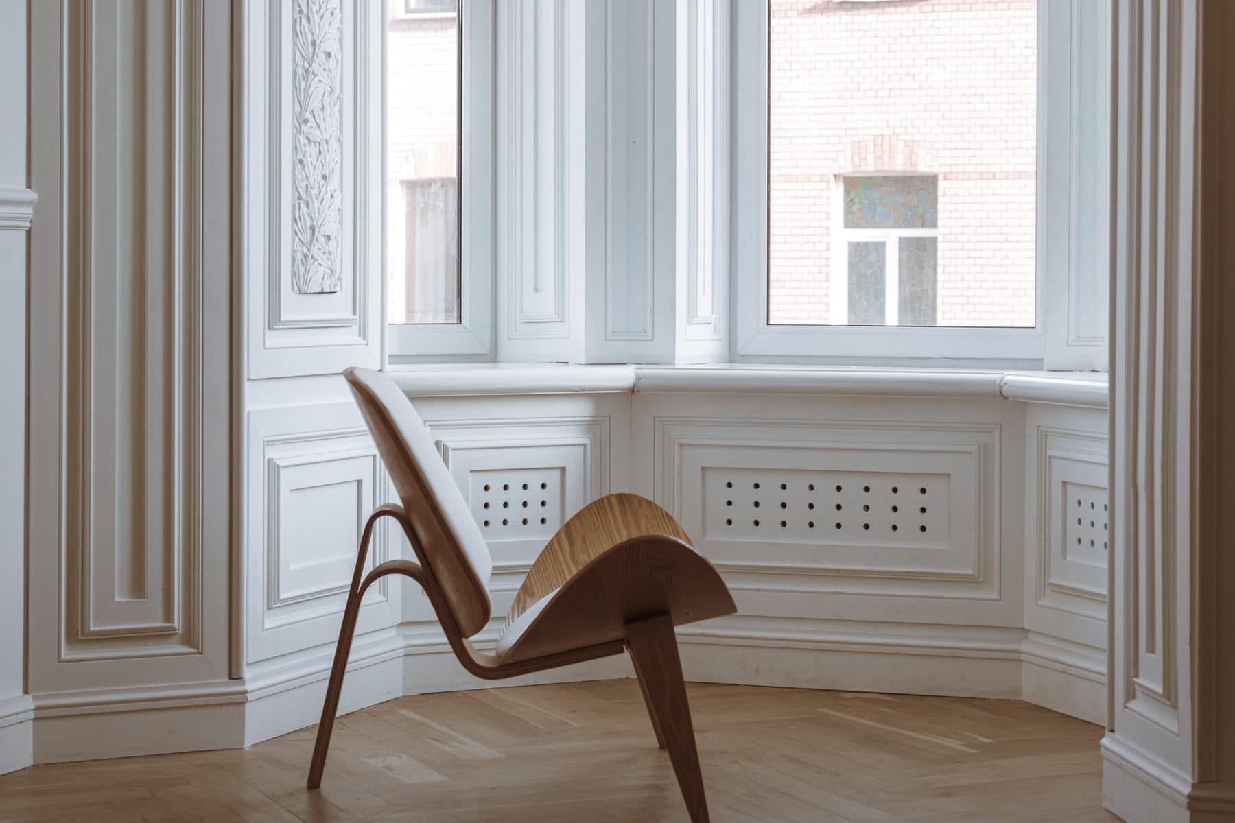 Nymalet lys stue med hvide stukpaneler, karnapvindue, sildebensgulv og skalstol i dansk design