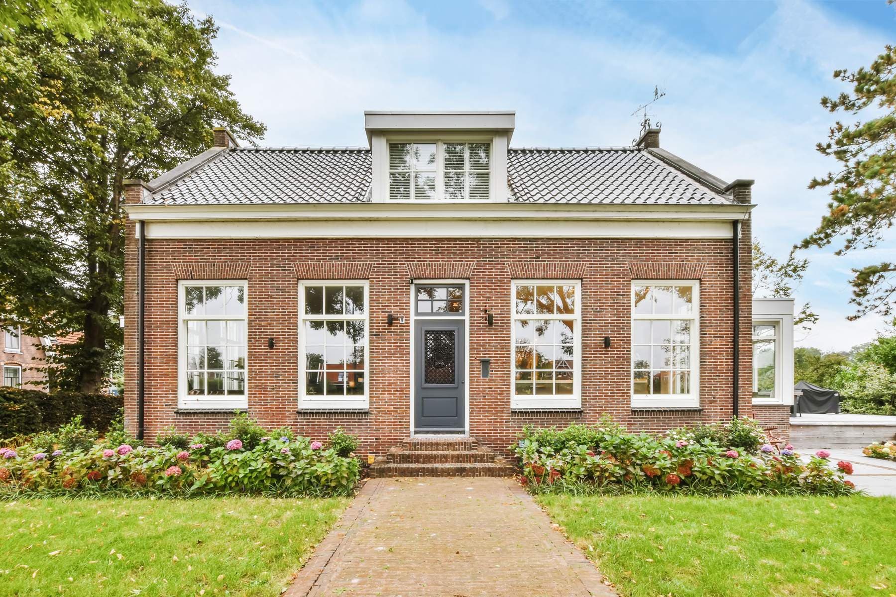Klassisk dansk muremestervilla i røde mursten med hvide sprossevinduer, kvist og blomstrende forhave