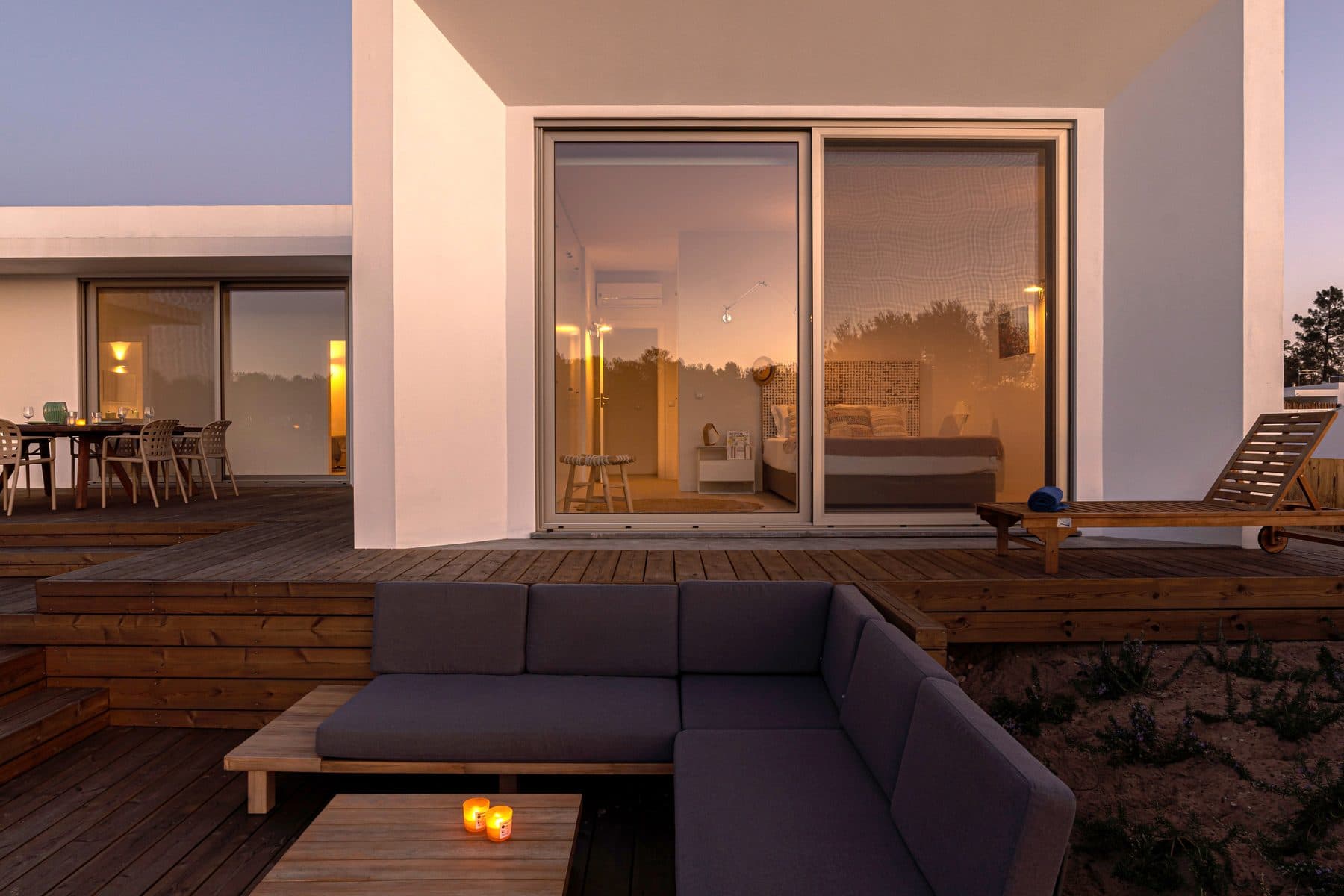 Træterrasse med loungemøbler foran et moderne hvidt hus i aftenlys
